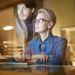 Mature and young colleagues watching attentively online conference in the evening